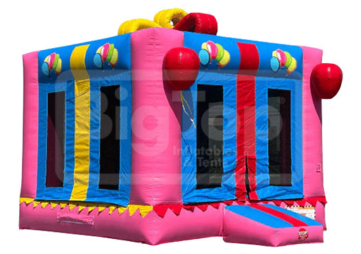 A pink inflatable bounce house designed to look like a giant pink gift box with multicolored accents and decorations, featuring mesh windows.