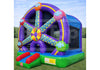 A colorful inflatable bounce house with a Ferris wheel design, featuring purple, blue, green, red, yellow, and pink sections, set up on a grassy field under a blue sky.