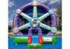 A large inflatable bouncy castle shaped like a Ferris wheel, featuring purple and blue sections with green, red, and yellow accents, set up outdoors on a blue ground cover with trees and sky in the background.