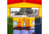 An inflatable bounce house viewed from inside, showing a bright orange and red ceiling, green and blue side walls, and a small window looking out onto a street with parked cars and trees.