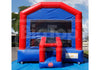 A red and blue inflatable bounce house with a clear front window and a small red slide, photographed outdoors on a blue ground cover with trees and sky in the background.