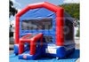 A red and blue inflatable bounce house with a slide, photographed outdoors on a blue tarp with trees and sky in the background.