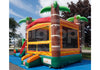 A tropical-themed inflatable bounce house with palm tree decorations, a slide, and a climbing wall, set up outdoors on a blue ground cover with trees and sky in the background.