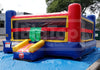 A large inflatable bounce house with a slide, photographed outdoors on a blue tarp. The structure is primarily blue, red, and yellow, with a clear front window and a green hanging decoration.