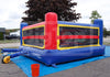 A large inflatable bounce house with a slide, photographed outdoors on a blue tarp. The structure is primarily blue, red, and yellow, with a clear front window and a green hanging decoration and back view.