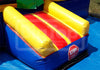A blue and yellow inflatable bouncy castle slide with red stripes, featuring a red octagonal stop sign on the side, set outdoors on a blue ground cover.