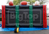 A large inflatable bounce house or play structure with a black center, red side walls, green vertical straps, and sports balls mounted on top, photographed outdoors on a blue tarp with trees and buildings in the background. A large 'BigTop Inflatable & Tents' watermark is visible across the front.