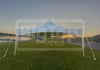 A large white canopy tent with a peaked roof is set up on a green lawn near a lake at sunset. A large semi-transparent 'BigTop Inflatable & Tents' watermark is overlaid across the center.