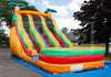 Colorful inflatable slide with palm tree designs on a blue mat outdoors.