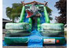 An inflatable bouncy castle slide with a crocodile design, featuring green inflatable walls, a blue slide floor, and a gray crocodile with an open mouth at the top, set outdoors on a blue tarp.