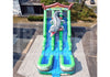 An inflatable water slide with a large crocodile figure on the slide, set up outdoors on a concrete surface with a white sheet underneath. The slide features green and blue sections, a ladder, and a splash pad at the bottom.