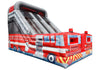 An inflatable fire truck bouncy castle with a large slide, featuring red, white, and blue graphics with yellow caution stripes.