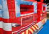 An inflatable bouncy castle designed to look like a red fire engine, featuring blue sky and white cloud patterns, set outdoors on a blue floor covering.